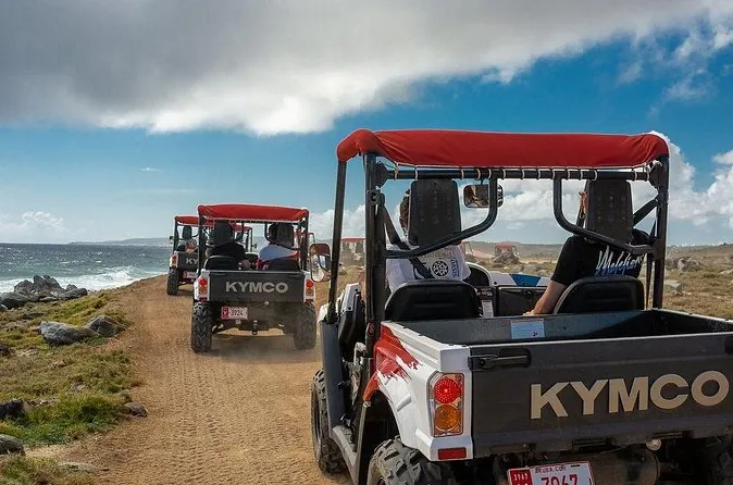 Two-seat UTVs parked on a dirt track by the sea