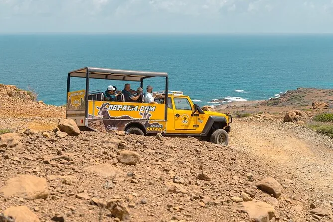 An open-top 4x4 safari vehicle on a rocky clifftop above the sea