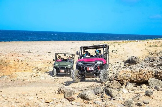 A convoy of orange multi-seat UTVs on a dusty road